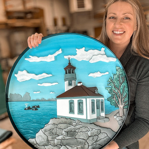 Custom scroll art of a landscape and lighthouse framed in a round black steel frame